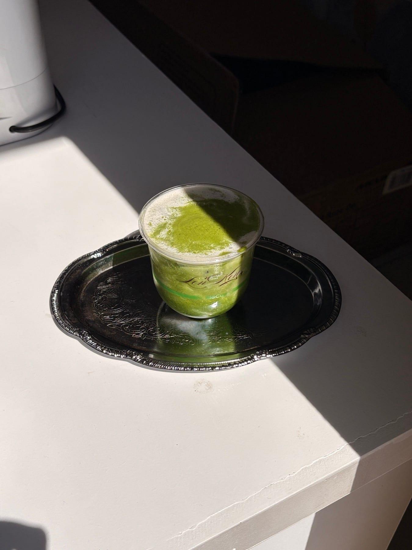 A frothed Lenken matcha on an engraved silver tray, caught in a hard band of afternoon sunlight.